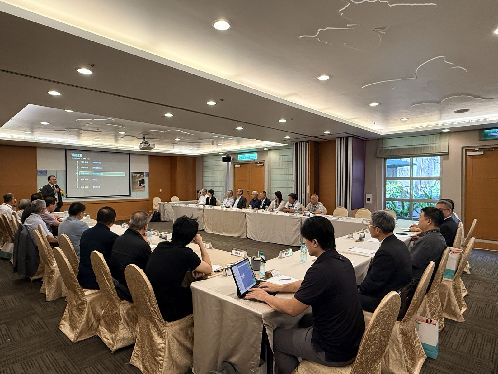 大師講座現場，講者於台前簡報，與會企業主管圍坐會議桌聆聽